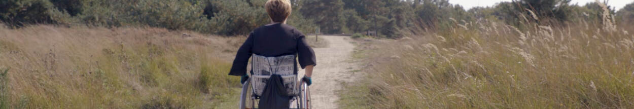 Mevrouw in een rolstoel maakt een ommetje door een natuurgebied.