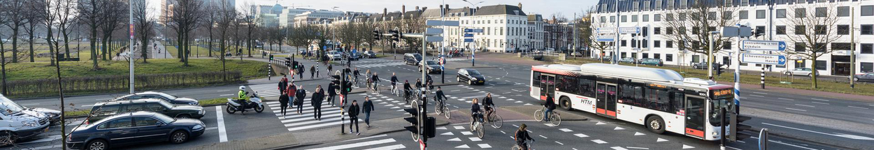 Kruispunt in Den Haag met verschillende voertuigen: auto's, fietsen, lijnbus en voetgangers.