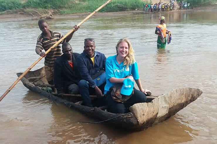 Vrouw en vier mannen in houten kano op modderige rivier