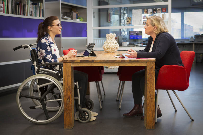 Een foto van twee vrouwen die een sollicitatiegesprek voeren, een van hen zit in een rolstoel.