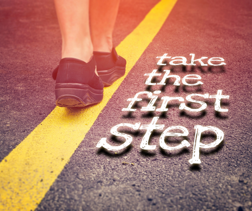 Op de foto zien we de benen van iemand die op een weg loopt. Er staat 'take the first step' op de foto.