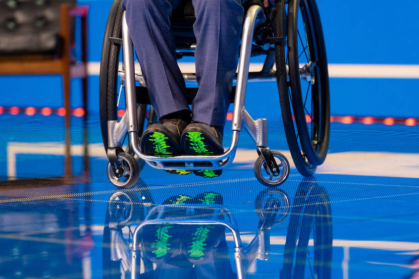 Persoon in rolstoel waarbij alleen de benen en schoenen zichtbaar zijn op knalblauwe vloer