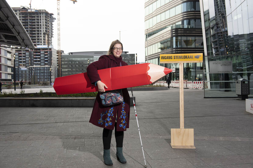 Vrouw met een enorm rood potlood vlakbij een stemlokaal