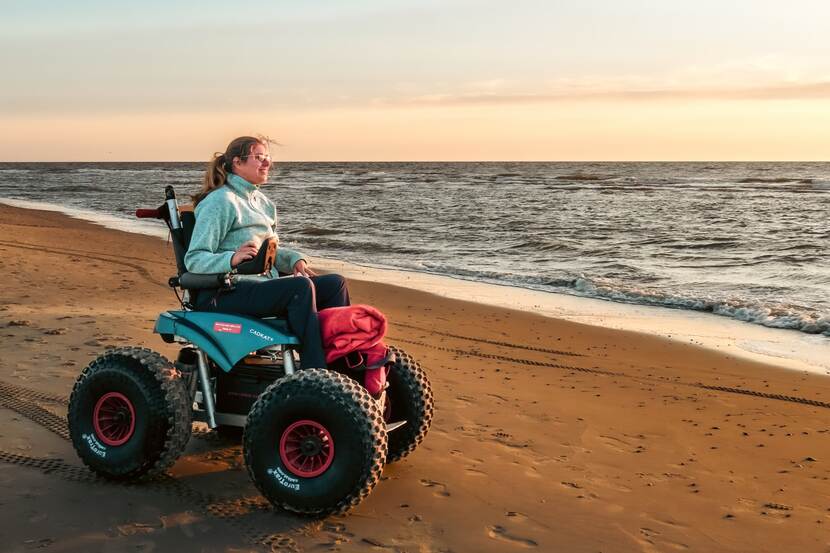 Een jonge vrouw maakt een wandeling in een rolstoel langs het strand