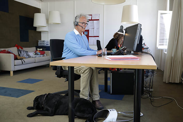 Een man achter een computer met een hond liggend op de vloer